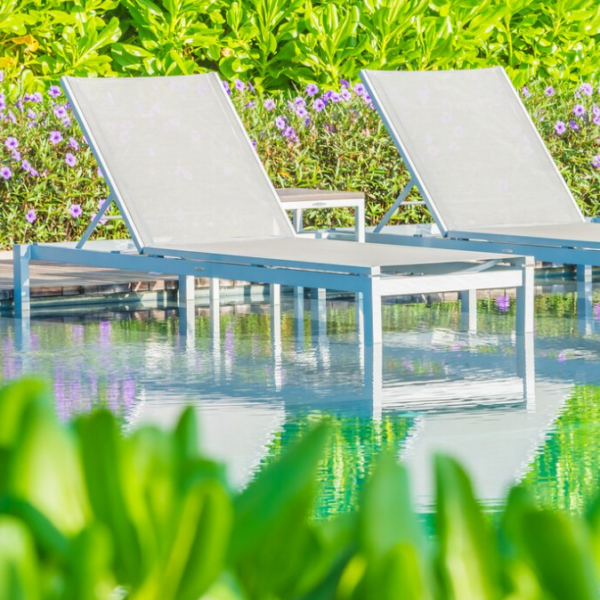 three pool chairs, flowers and bushes behind, the pool and flowers in front of it