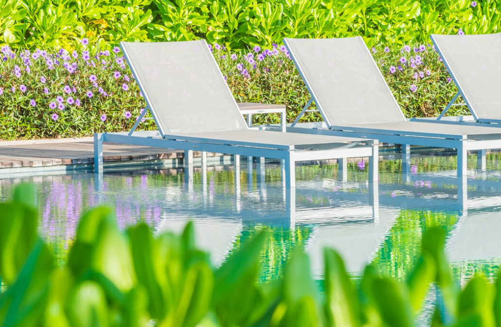 three pool chairs, flowers and bushes behind, the pool and flowers in front of it