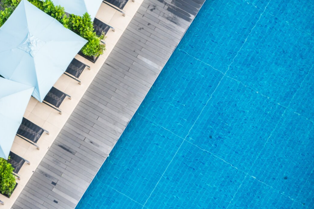 blue swimming pool, pool chairs, and light blue sun umbrellas over it