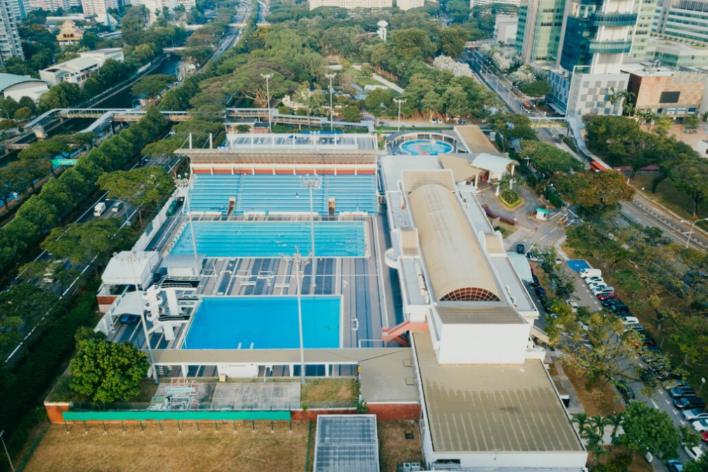 aerial view of sports center, pools, trees, and city buildings