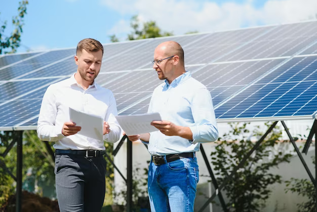 Two men with papers in their hands talking against the backdrop of solar panels