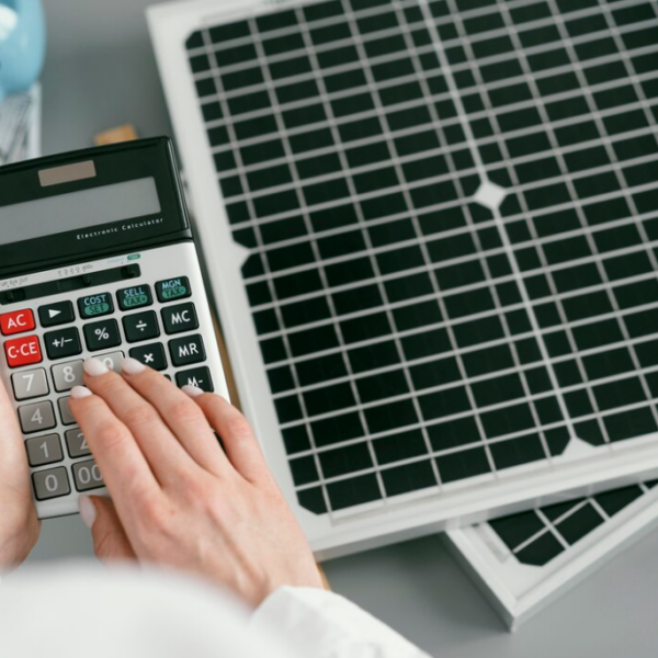 woman holds a calculator, the biggy bank with dollar bills, solar panels on the gray table