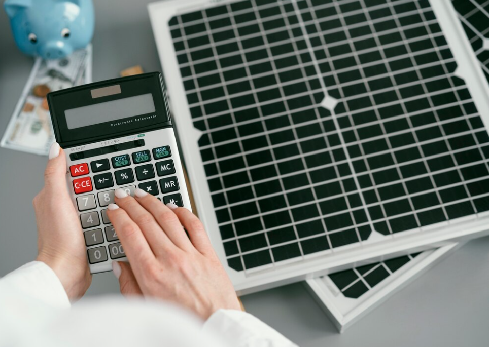 woman holds a calculator, the biggy bank with dollar bills, solar panels on the gray table